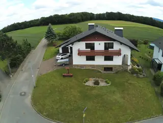 Luftaufnahme des Ferienhauses Werra-Ausblick mit großem Garten, Holzbalkon und weitem Blick auf Felder und Wälder.