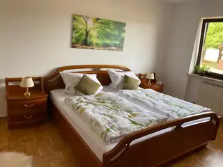 Gemütliches Doppelzimmer mit Holzbett, floraler Bettwäsche und großem Waldbild über dem Kopfteil.