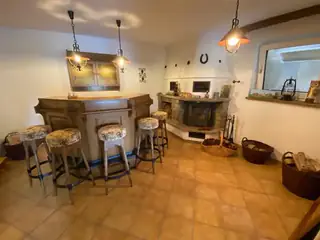 Rustikale Hausbar aus dunklem Holz mit Barhockern und traditionellem Kaminofen in gemütlicher Atmosphäre.
