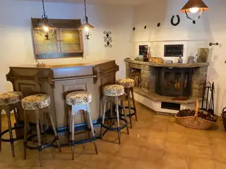 Einladende Hausbar mit verzierter Holztheke, floralen Barhockern und traditionellem Steinkamin mit Kaminfeuer.