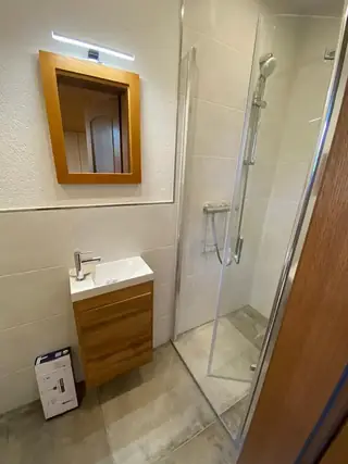 Kompaktes modernes Badezimmer mit Glasdusche, Holzwaschtisch und beleuchtetem Wandspiegel.