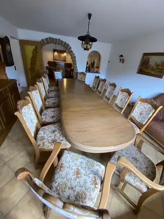 Langer ovaler Esstisch mit floral gepolsterten Stühlen in einem rustikalen Esszimmer mit Steinbogen und Hausbar im Hintergrund.
