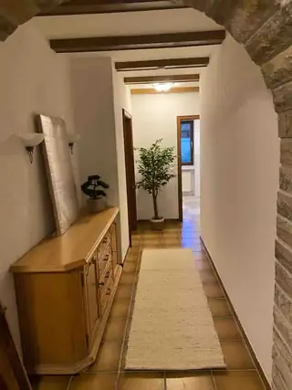 Langer Flur mit Terrakottafliesen, Läufer, rustikalen Deckenbalken und Sideboard aus hellem Holz.