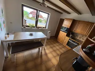 Rustikale Wohnküche mit Holzschränken, modernem Einbau-Backofen, Esstisch und Panoramafenster.