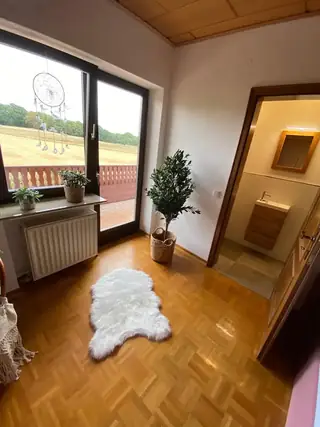 Heller Flur mit Parkettboden, weißem Fellteppich, Balkontür mit Feldblick und angrenzendem Gäste-WC.