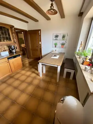 Rustikale Küche mit Holzbalkendecke, Terrakottafliesen, Esstisch mit Bänken und Kräuterbildern an der Wand.