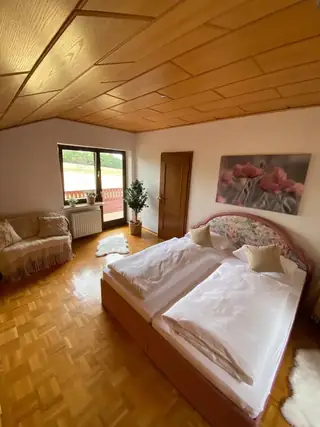 Helles Schlafzimmer mit Doppelbett, dekorativer Holzdecke, Parkettboden und direktem Zugang zum Balkon.